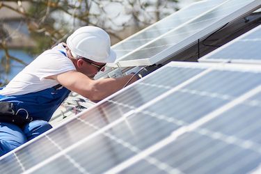 Zu sehen ist ein Mann, der eine Solaranlage auf einem Dach wartet.